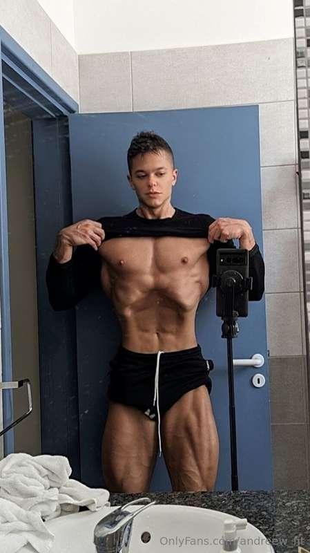 Flexing hard in the mirror, shirt lifted to show off chest a..
