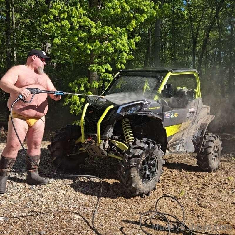Pressure washing in a yellow jockstrap and muck boots
